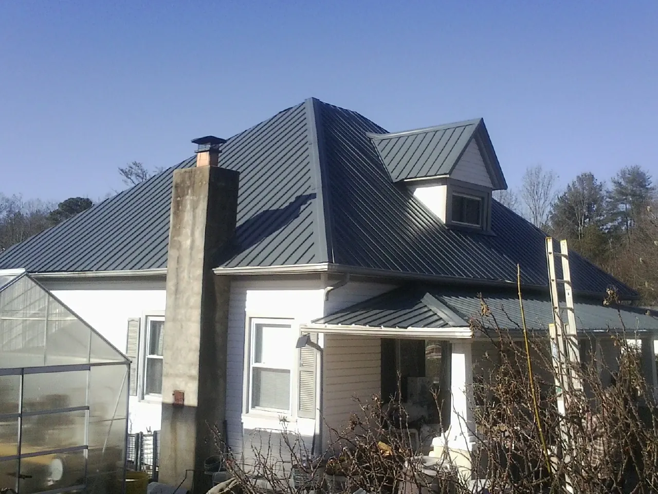 Dark blue standing seam metal roof on a white farmhouse with dormer — Slate & Tile Roof Repair by Roofing Brothers in Voorheesville