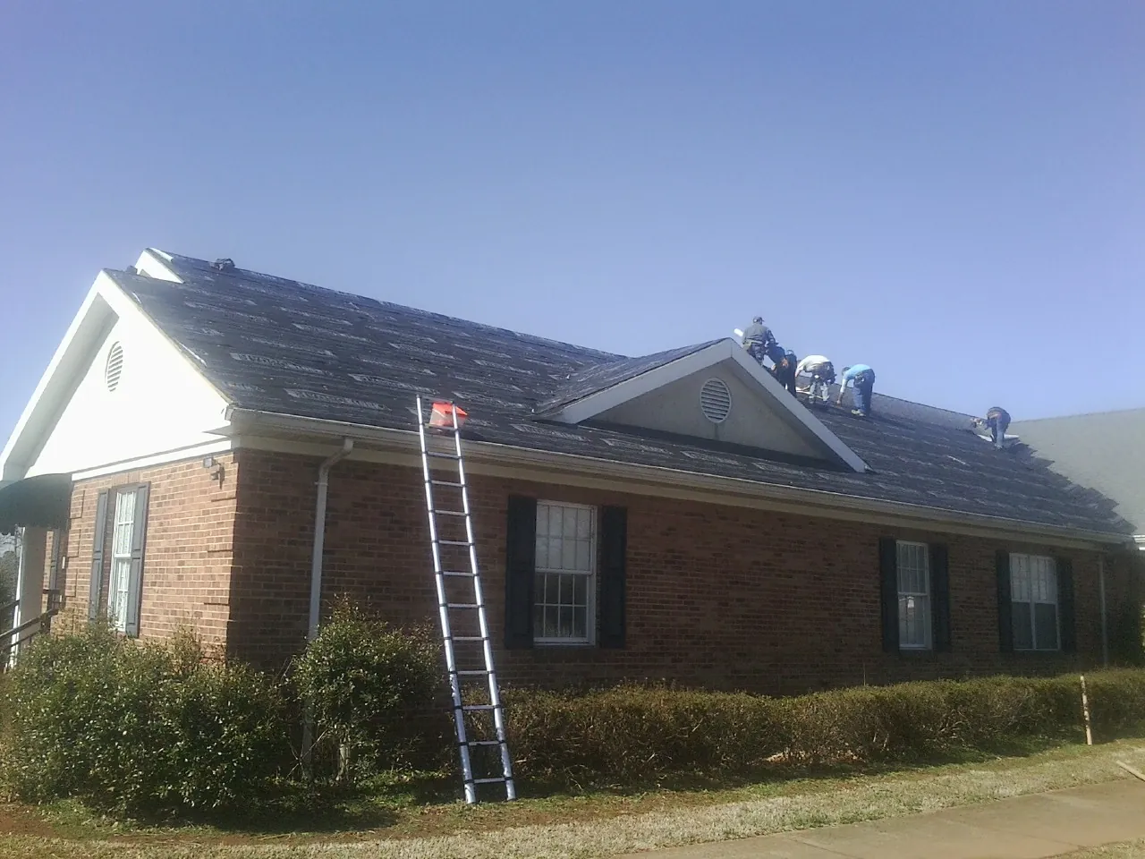 Crew tearing shingles off a brick ranch roof with a ladder set — Emergency Roof Repair work by our crew in Voorheesville