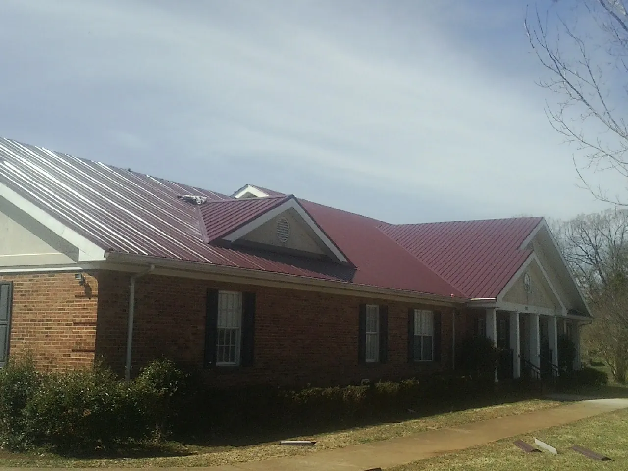 Red metal roof with gabled entries on a long brick building, from a Hail Damage Roof Repair job in Voorheesville