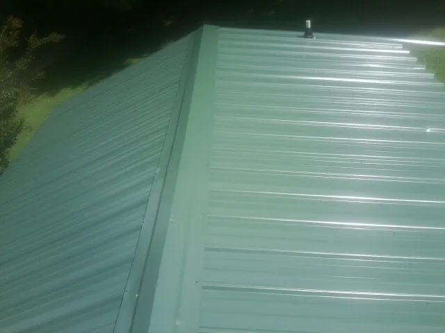 New green metal panels meeting at the ridge of a roof — Flat Roof Repair work by our crew in Voorheesville