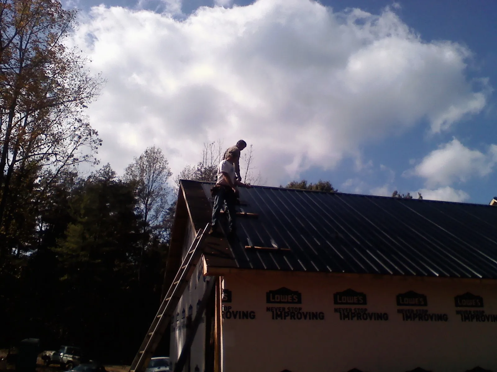 Roofer fastening dark metal panels high against a cloudy sky, from a Roof Inspection job in Voorheesville