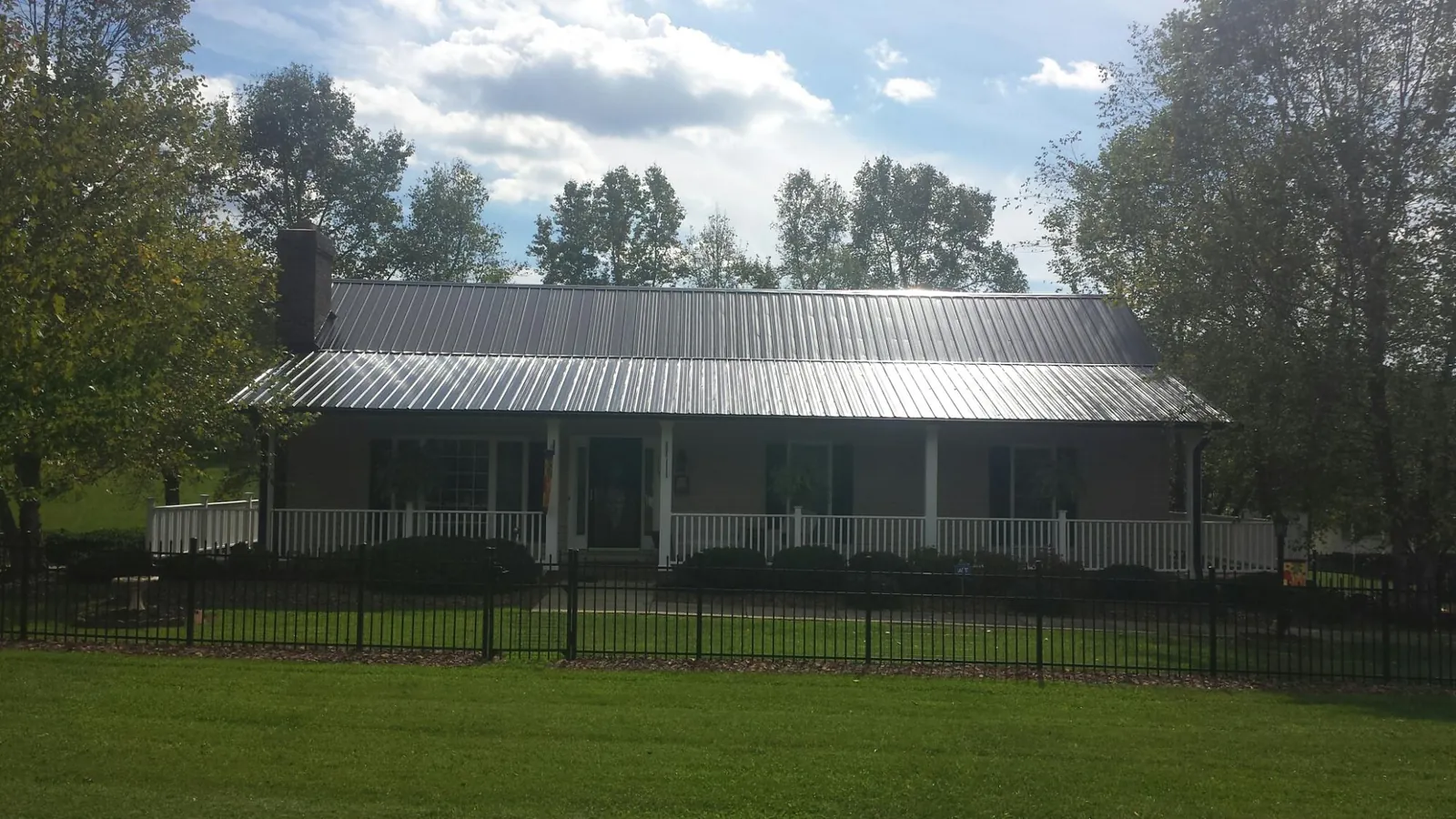 Gray metal roof on a brick ranch with a full width front porch — Gutter Guard Installation work by our crew in Voorheesville