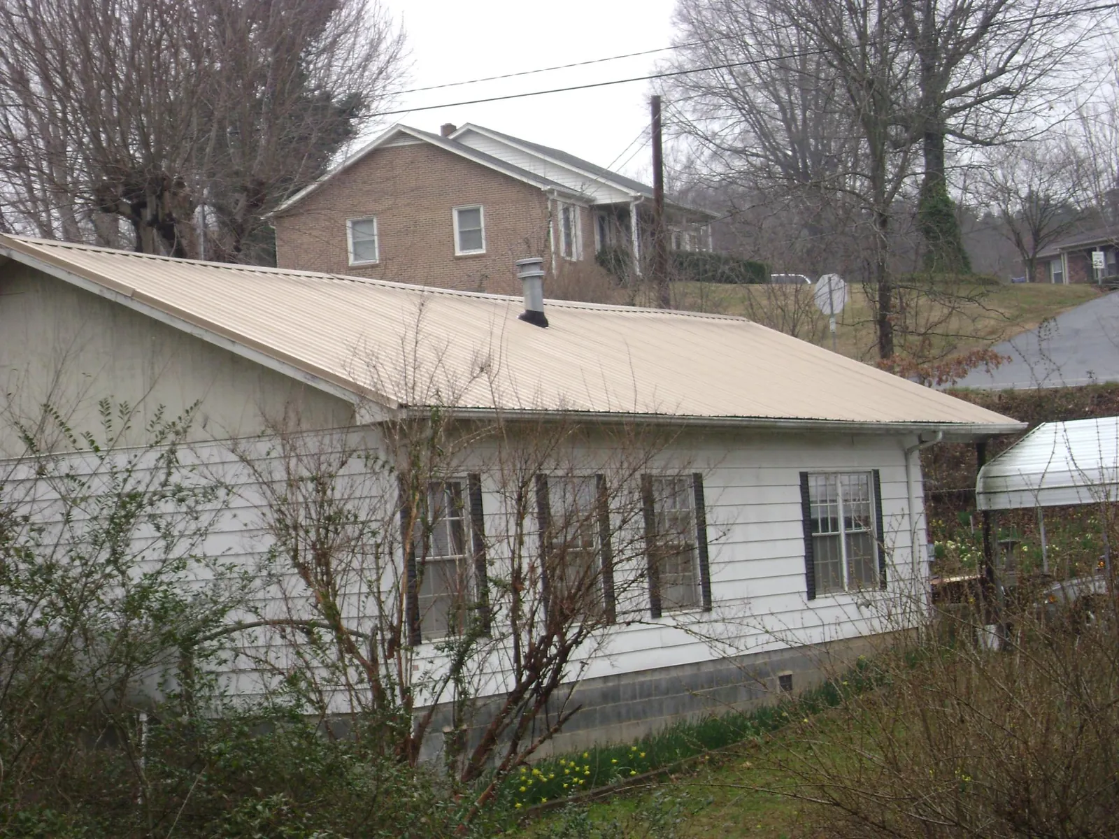 Tan metal roof on a white sided house set into a hillside — Commercial Roofing by Roofing Brothers in Voorheesville